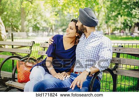 Picture - Indian couple hugging on bench in urban park. Fotosearch
