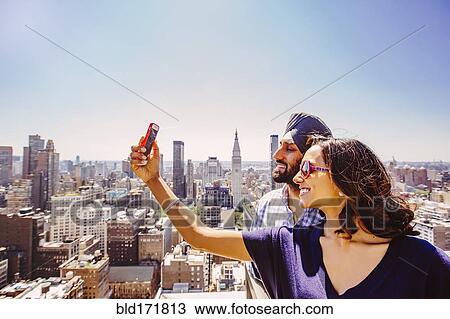 Stock Image - Indian couple taking selfie over New York cityscape, New York, United States. Fotosearch
