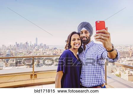Stock Photography - Indian couple taking selfie over New York cityscape, New York, United States. Fotosearch