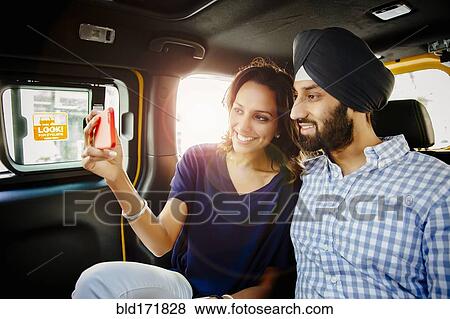 Stock Photo - Indian couple taking selfie with cell phone in taxi. Fotosearch