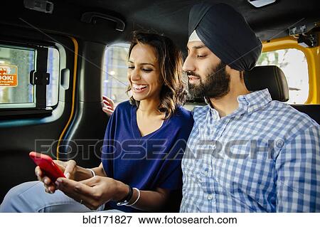 Stock Photo - Indian couple using cell phone in taxi. Fotosearch
