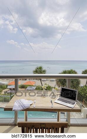 Stock Photography - Laptop on restaurant balcony table overlooking beach. Fotosearch