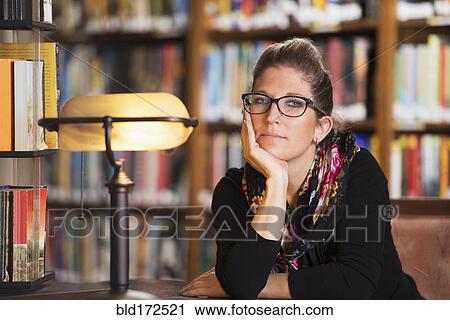 Stock Image - Librarian sitting at desk in library. Fotosearch