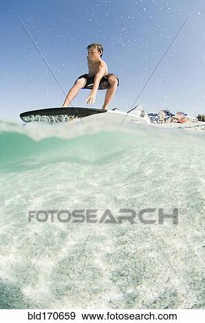 Low angle view of man standing on surfboard View Large Photo Image Stock Photo - Low angle view of man standing on surfboard. Fotosearch