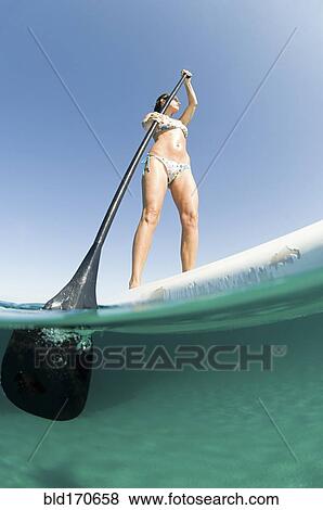 Low angle view of woman standing on paddle board View Large Photo Image Stock Photo - Low angle view of woman standing on paddle board. Fotosearch