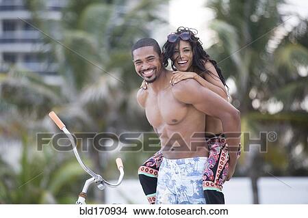 Picture - Man carrying girlfriend piggyback on urban beach. Fotosearch