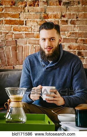 Stock Photograph - Man drinking coffee on sofa in living room. Fotosearch