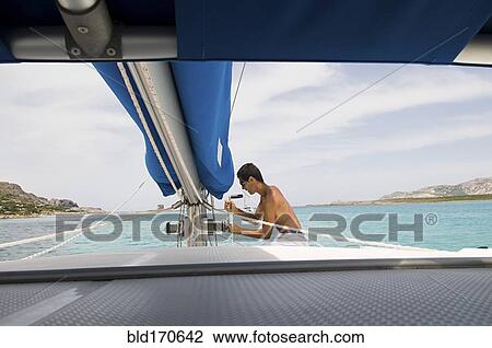 Stock Image - Man hoisting sailboat rigging on deck. Fotosearch