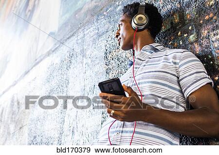 Stock Photo - Man listening to cell phone by mural. Fotosearch