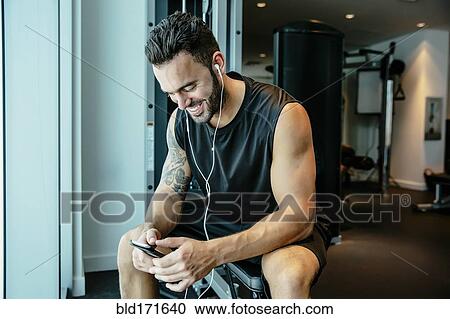 Man listening to earbuds in gymnasium View Large Photo Image Stock Image - Man listening to earbuds in gymnasium. Fotosearch
