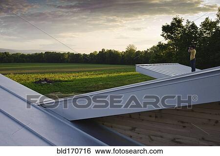 Stock Photograph - Man on roof admiring view of rural field. Fotosearch