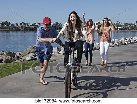 Picture - Man pushing woman on bicycle at waterfront. Fotosearch