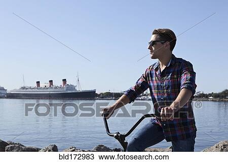 Stock Image - Man riding bicycle at waterfront. Fotosearch