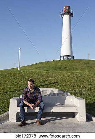 Stock Photo - Man sitting on park bench near lighthouse. Fotosearch