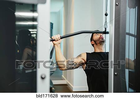 Stock Photo - Man using exercise machine in gymnasium. Fotosearch