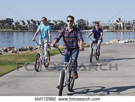 Stock Image - Men riding bicycles at waterfront. Fotosearch