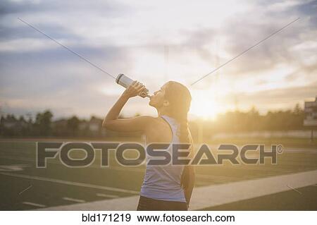 Stock Photo - Mixed race athlete drinking water bottle on sports field. Fotosearch