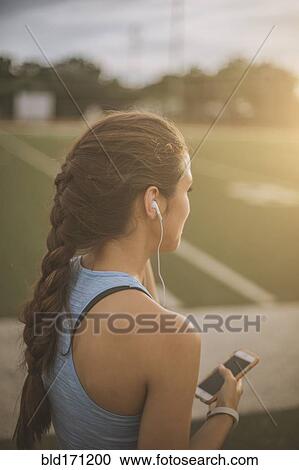 Stock Image - Mixed race athlete listening to mp3 player on sports field. Fotosearch