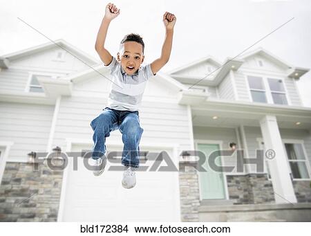 Picture - Mixed race boy jumping for joy in driveway. Fotosearch