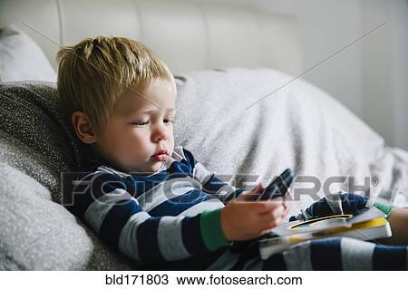 Stock Image - Mixed race boy playing with cell phone on bed. Fotosearch