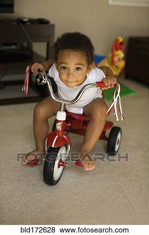 Stock Photo - Mixed race boy riding tricycle in living room. Fotosearch