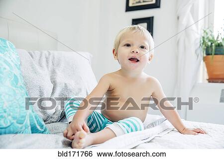 Stock Photograph - Mixed race boy sitting on bed. Fotosearch