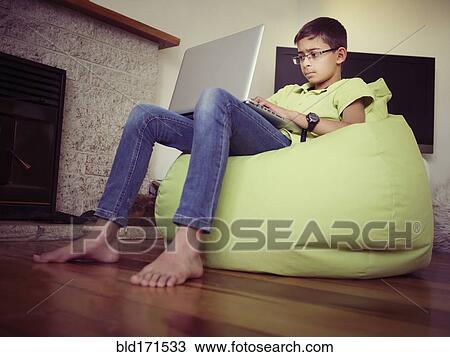 Stock Image - Mixed race boy using laptop in bean bag. Fotosearch