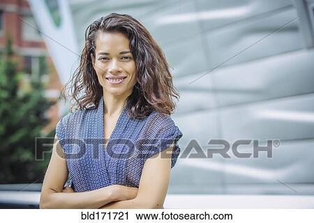 Stock Image - Mixed race businesswoman standing with arms crossed outdoors. Fotosearch
