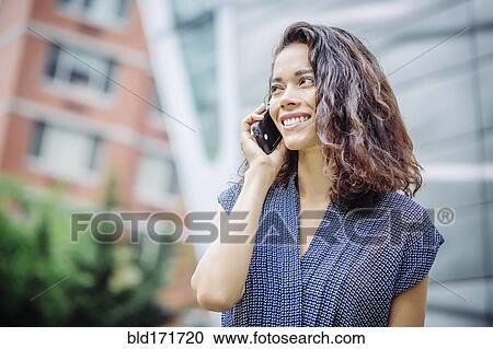 Stock Image - Mixed race businesswoman talking on cell phone outdoors. Fotosearch