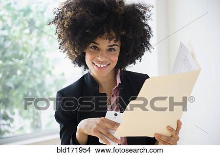 Picture - Mixed race businesswoman using cell phone near window. Fotosearch