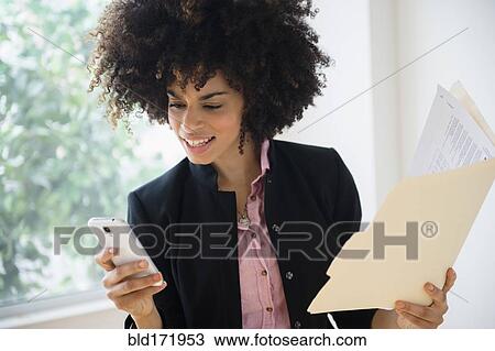 Stock Image - Mixed race businesswoman using cell phone near window. Fotosearch