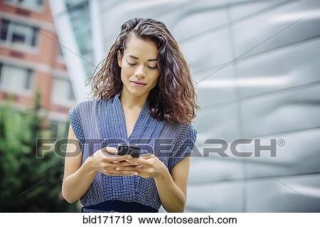 Stock Photo - Mixed race businesswoman using cell phone outdoors. Fotosearch