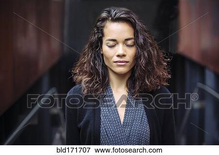 Stock Photo - Mixed race businesswoman with eyes closed in office. Fotosearch