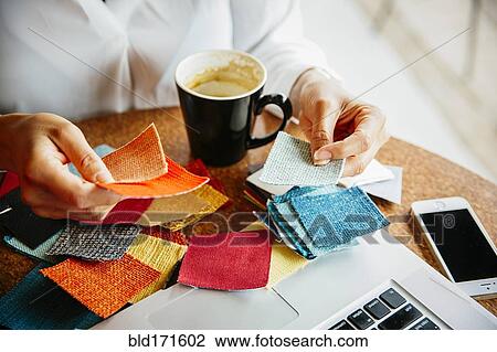 Stock Image - Mixed race designer examining fabric swatches. Fotosearch