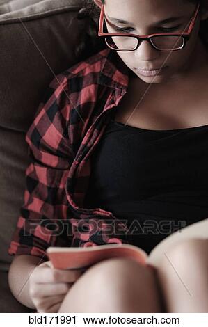 Stock Image - Mixed race girl reading on sofa. Fotosearch
