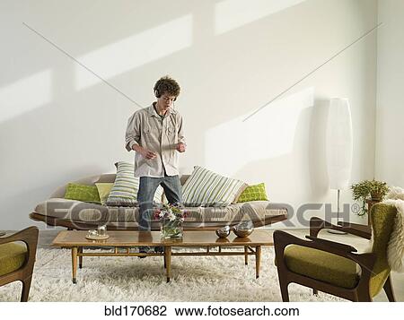 Stock Image - Mixed race man listening to headphones in living room. Fotosearch