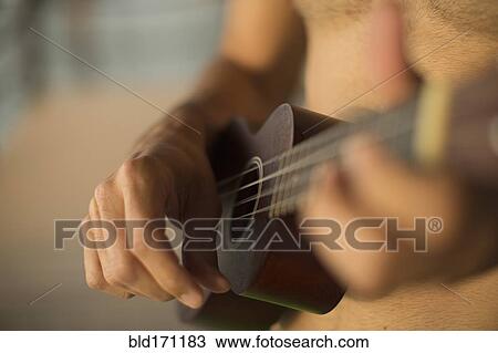 Stock Image - Mixed race man playing ukulele on beach. Fotosearch