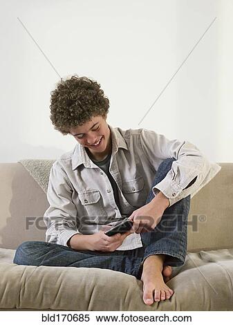Stock Photography - Mixed race man using cell phone on sofa. Fotosearch