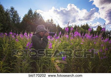 Stock Image - Mixed race photographer photographing flowers. Fotosearch