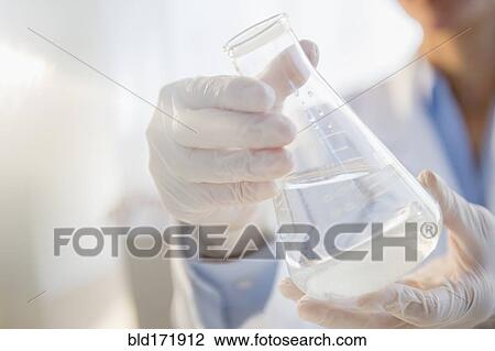 Stock Image - Mixed race scientist examining beaker in laboratory. Fotosearch