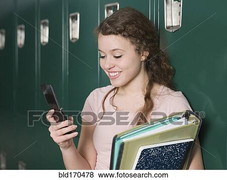 Stock Photo - Mixed race student using cell phone by locker in school hallway. Fotosearch