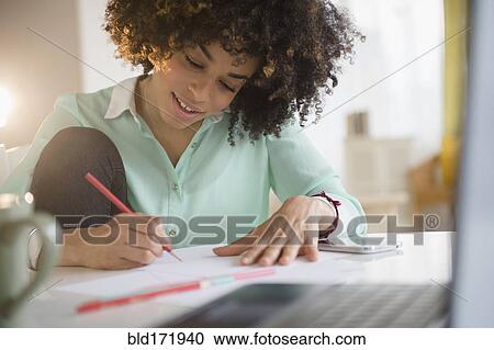 Stock Image - Mixed race student writing notes at desk. Fotosearch