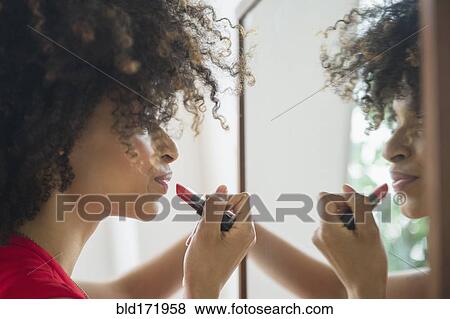 Stock Photo - Mixed race woman applying lipstick in mirror. Fotosearch