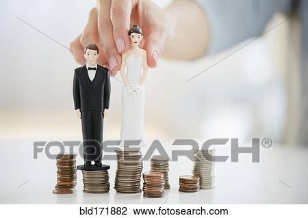 Stock Image - Mixed race woman balancing bride and groom statues on coin stacks. Fotosearch