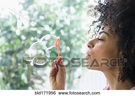 Stock Photograph - Mixed race woman blowing bubbles. Fotosearch