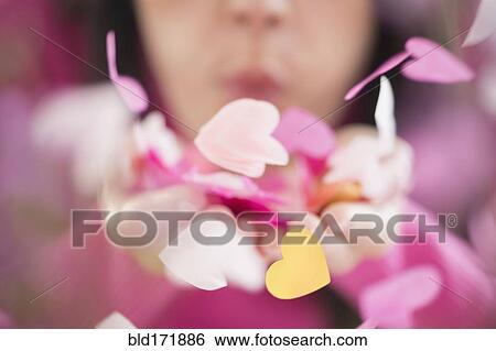 Stock Photograph - Mixed race woman blowing confetti hearts. Fotosearch