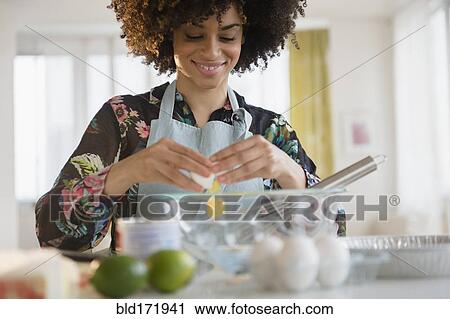 Stock Image - Mixed race woman cracking egg. Fotosearch