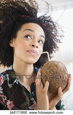 Stock Image - Mixed race woman drinking coconut water with straw. Fotosearch