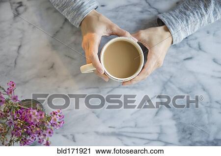 Stock Image - Mixed race woman drinking cup of coffee at table. Fotosearch