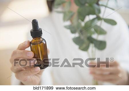 Mixed race woman holding bottle of essential oil View Large Photo Image Stock Photo - Mixed race woman holding bottle of essential oil. Fotosearch